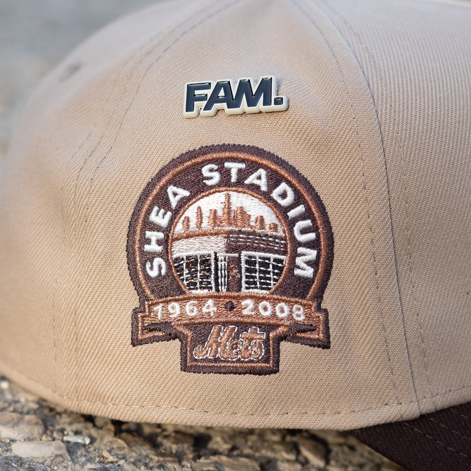 Beige cap with Shea Stadium patch and 'FAM' logo on a stone surface